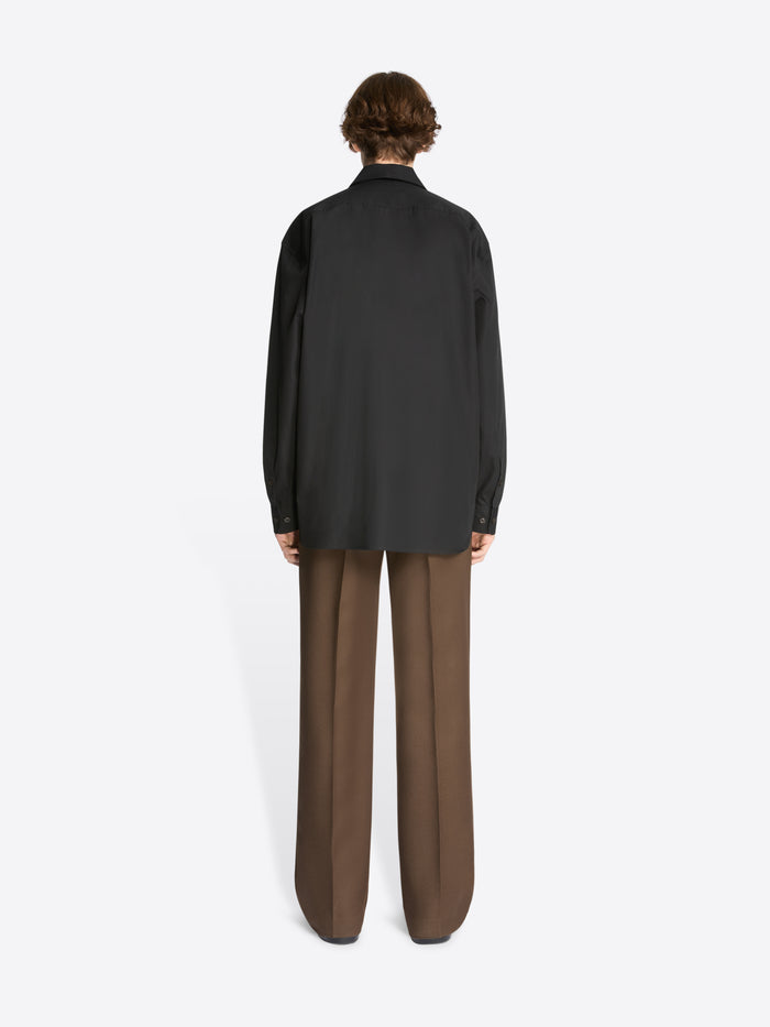 Backside of a model wearing a black cotton shirt and brown pants on a white background