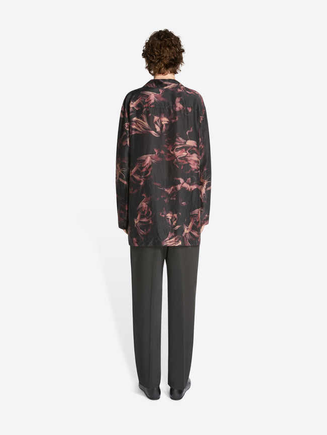 Backside of a model wearing a black and old rose colored popover silk shirt and black pants on a white background