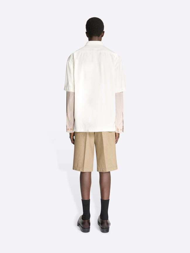 Backside of a model wearing an off white colored contrast sleeves denim shirt and beige shorts on a white background