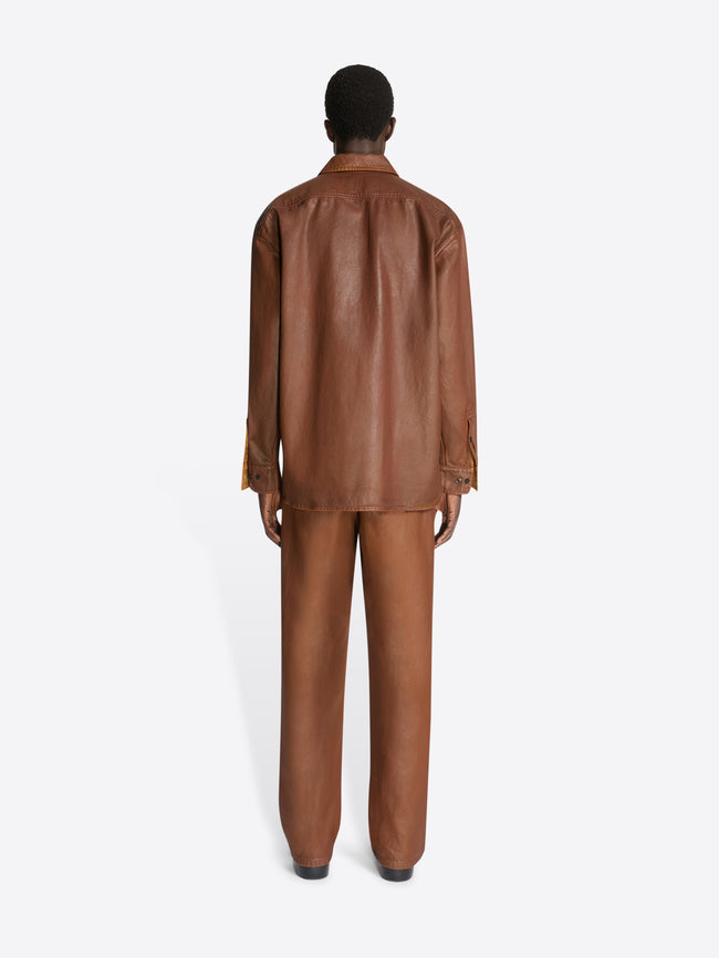 Backside of a model wearing a rust colored coated zipped shirt and matching pants on a white background