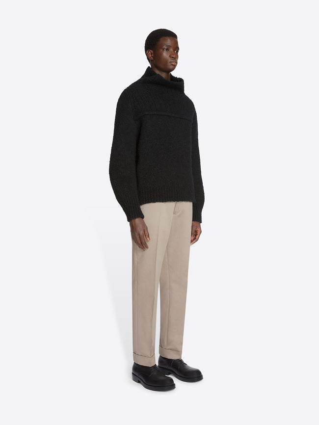 Model wearing a black sweater and cement colored cuffed pants on a white background