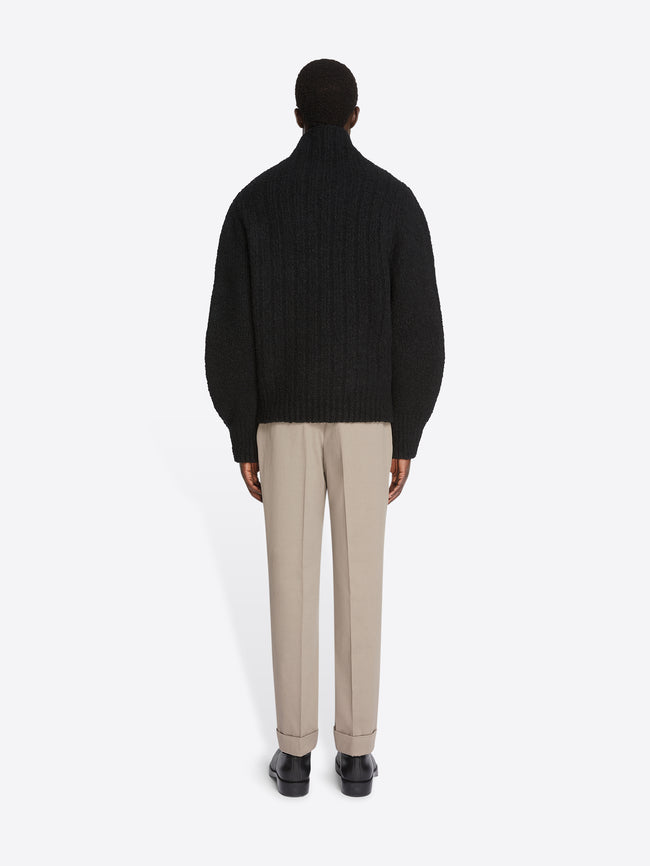 Backside of a model wearing a black sweater and cement colored cuffed pants on a white background