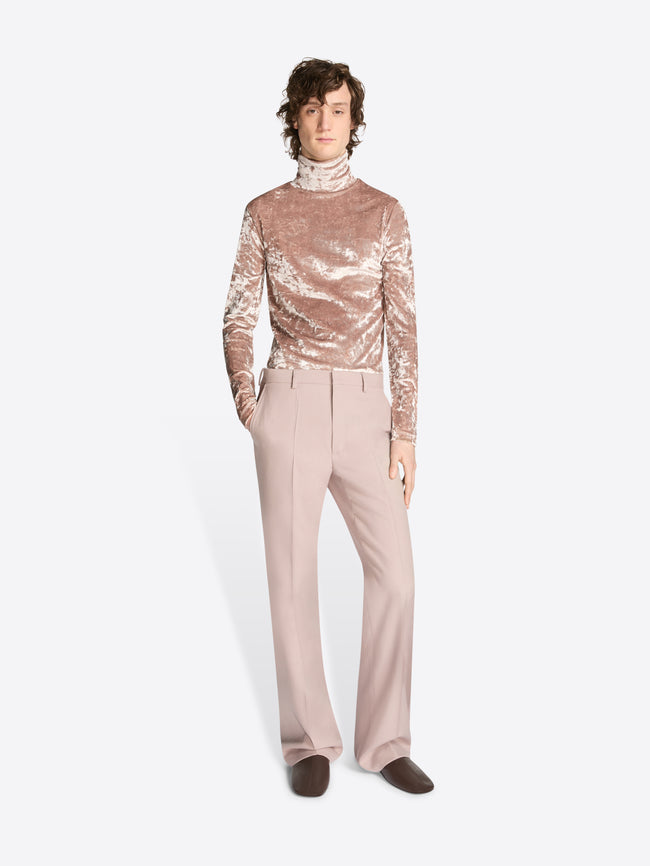 Person wearing a rose gold sequin top and beige pants on a white background
