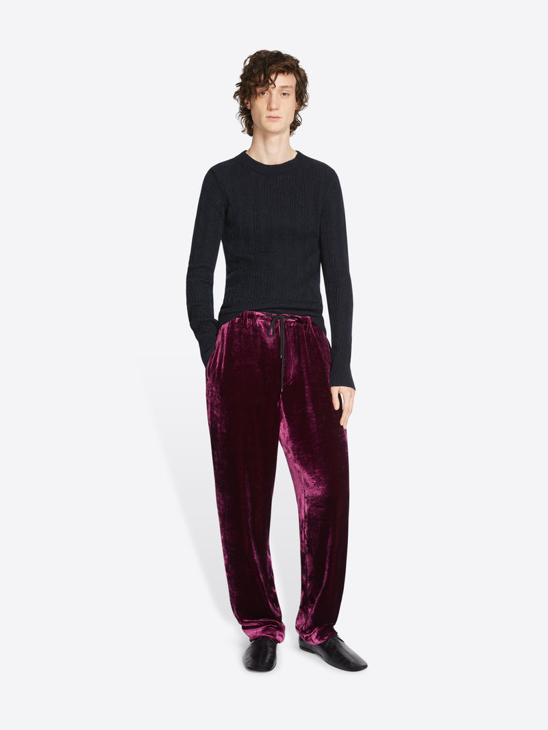 Person wearing a black sweater and burgundy velvet pants on a white background
