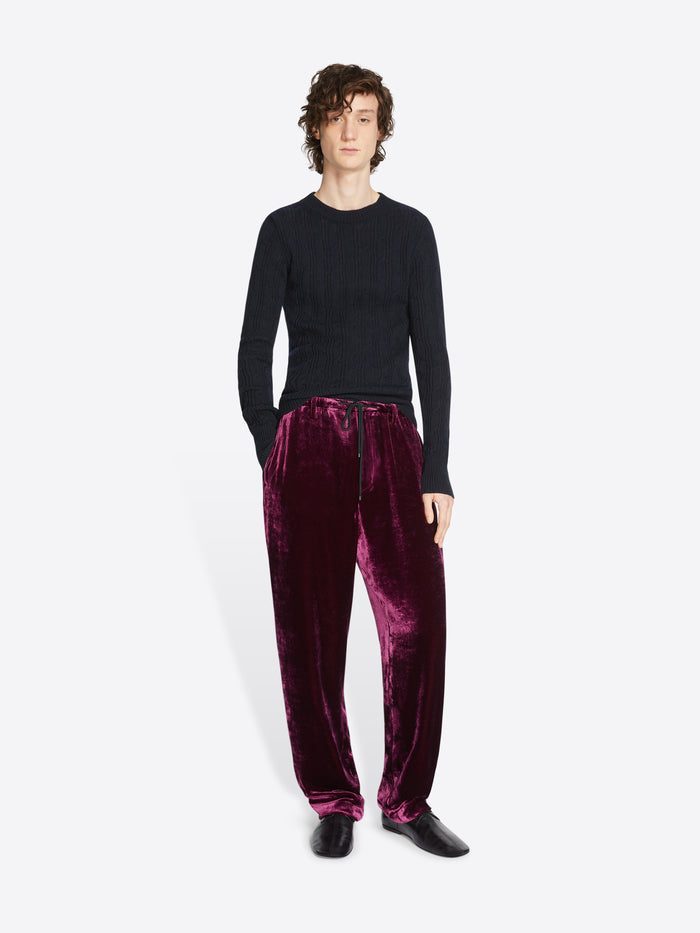 Person wearing a black sweater and burgundy velvet pants on a white background
