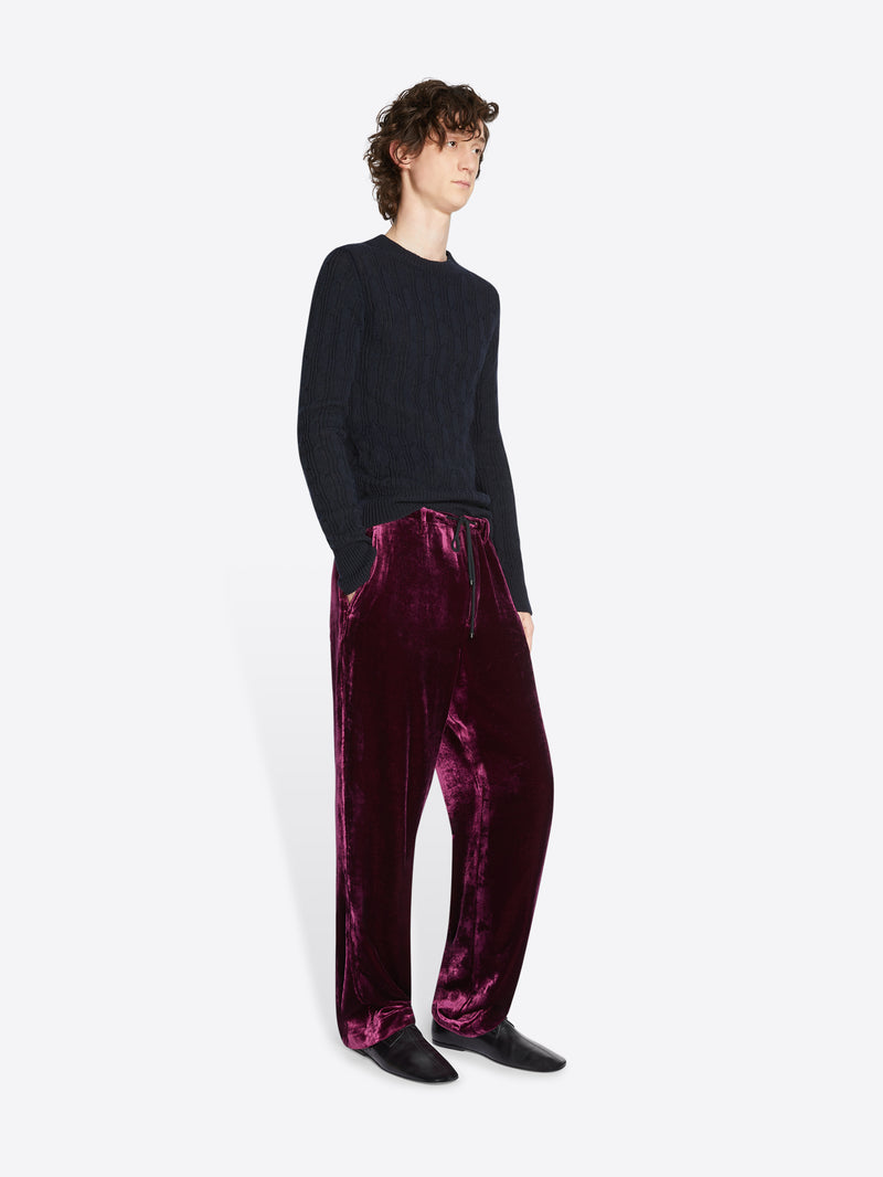 Person wearing a black sweater and burgundy velvet pants on a white background