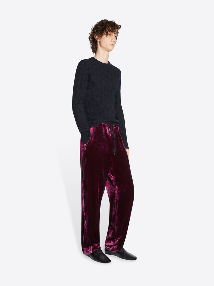 Person wearing a black sweater and burgundy velvet pants on a white background