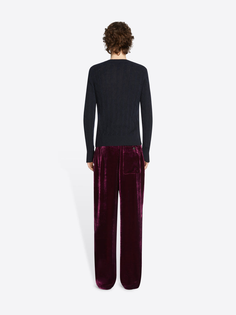 Person wearing a black long-sleeve top and burgundy velvet pants on a white background