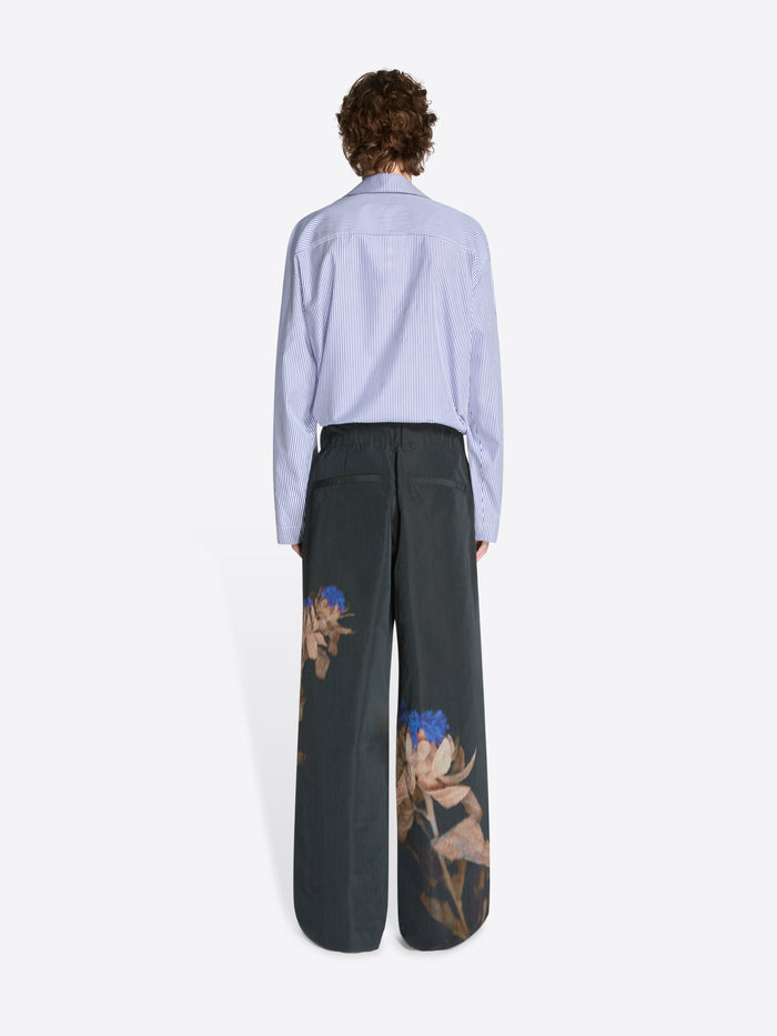 Backside of a model wearing a navy and white patterned shirt and black pleated pants with floral pattern on a white background