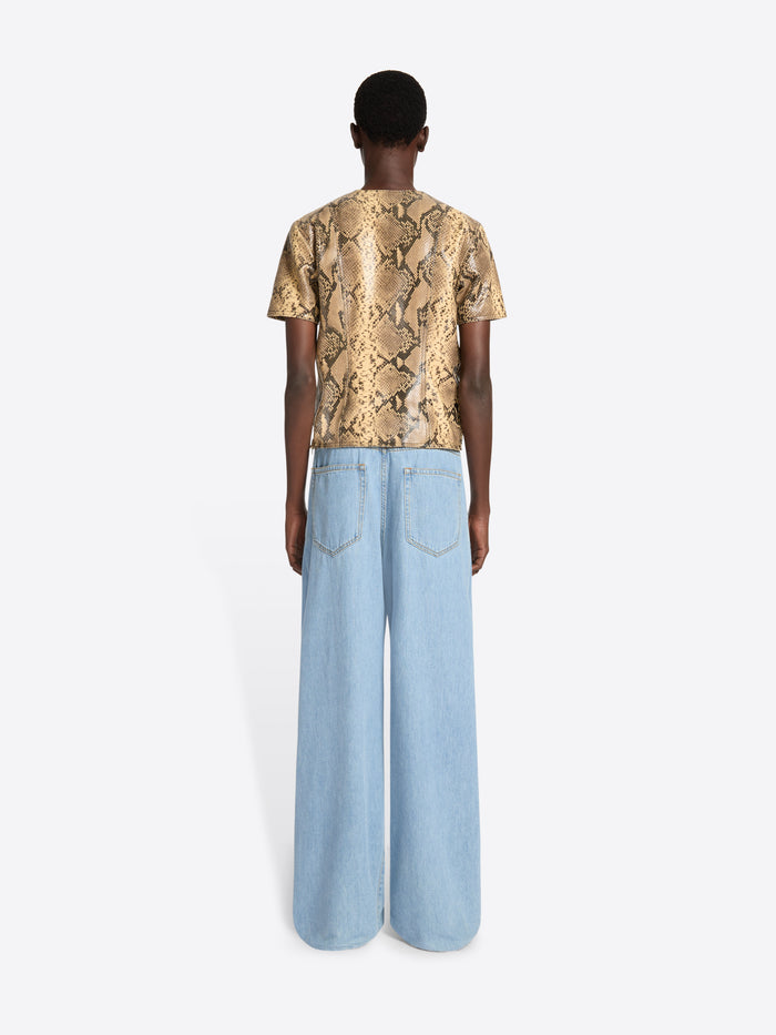 Person wearing a gold patterned shirt and light blue jeans on a white background