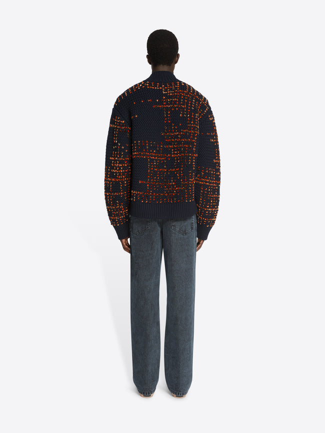 Backside of a model wearing a navy and orange patterned sweater and petrol colored loose fit jeans on a white background