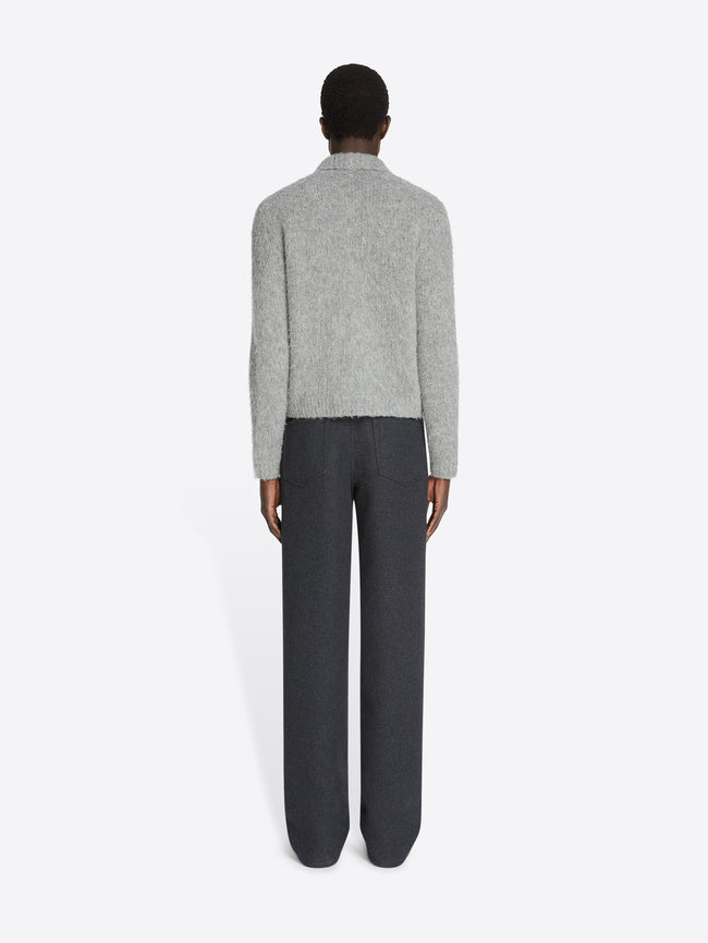 Person wearing a gray sweater and dark pants on a white background