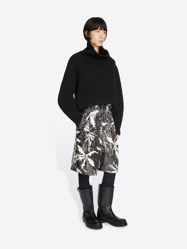 Model wearing a black sweater and black and white printed bermuda shorts on a white background