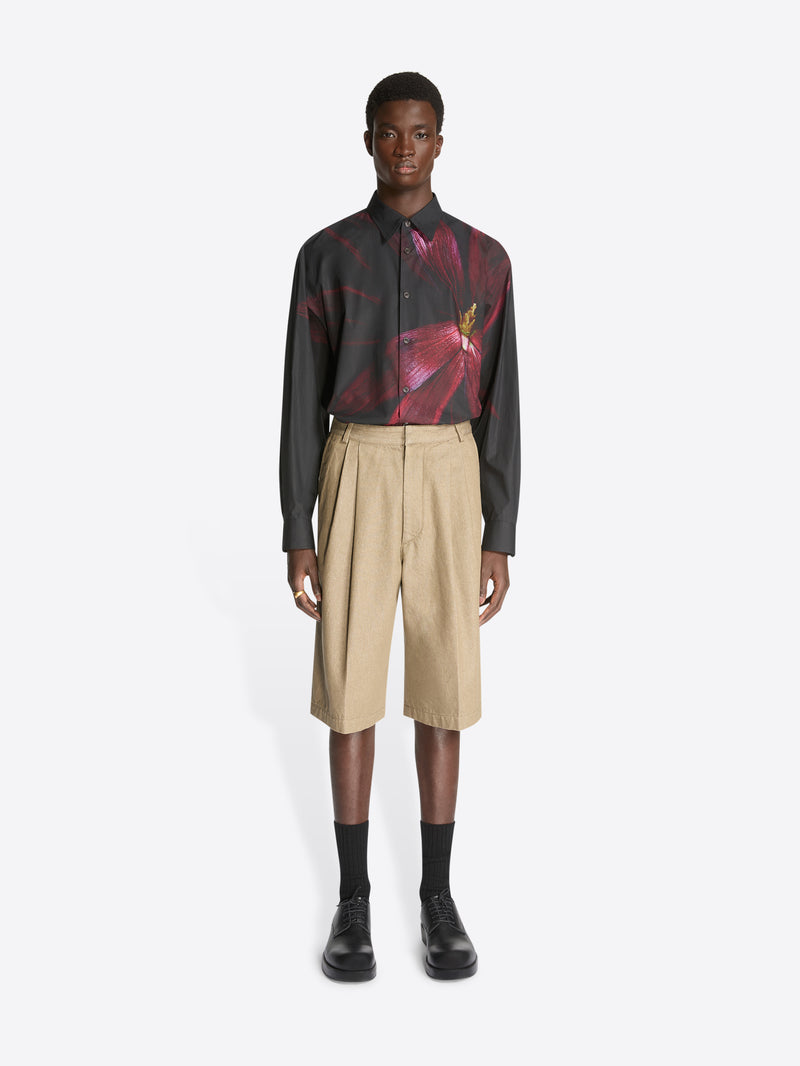 Model wearing a black shirt with burgundy flower print and a pair of stone colored tailored denim shorts on a white background