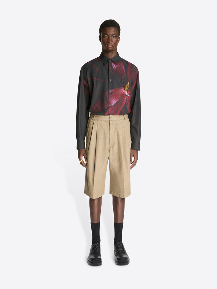 Model wearing a black shirt with burgundy flower print and a pair of stone colored tailored denim shorts on a white background