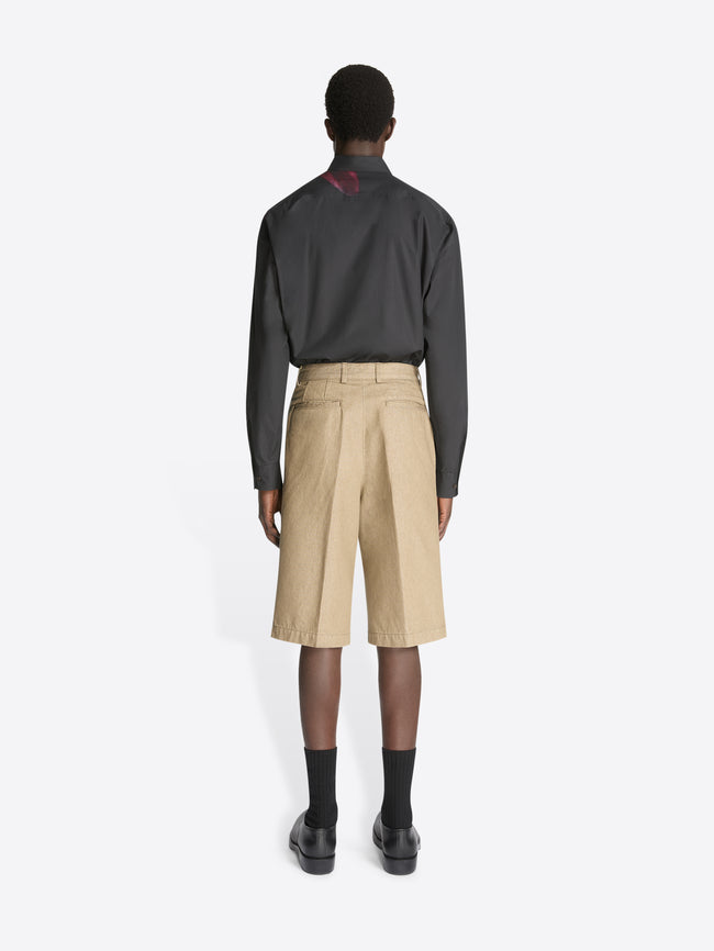 Backside of a model wearing a black shirt with burgundy flower print and a pair of stone colored tailored denim shorts on a white background