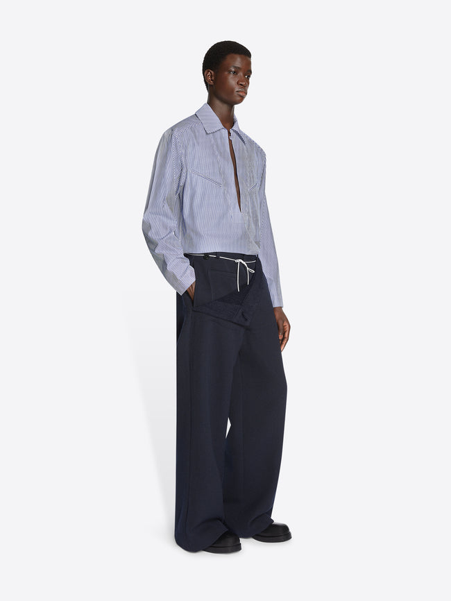 Person wearing a light blue shirt and dark pants on a white background
