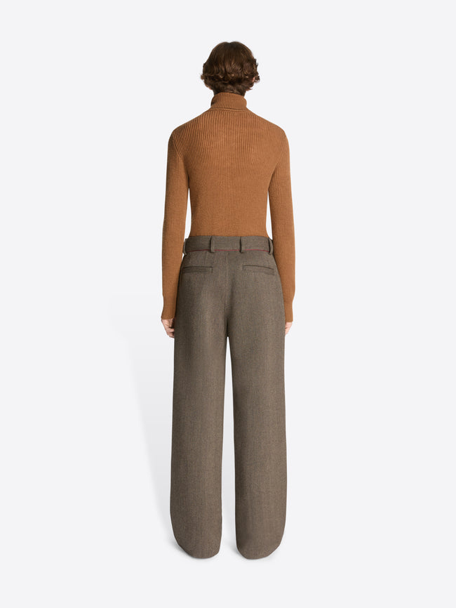 Person wearing a brown sweater and gray pants on a white background