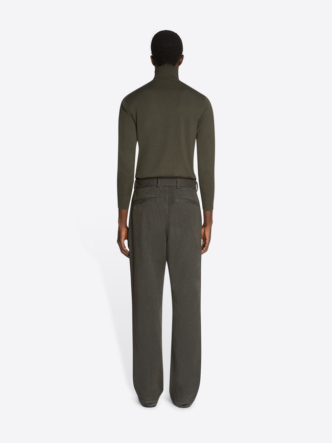 Backside of a model wearing a green turtleneck and a pair of dark grey overdyed sailor pants on a white background