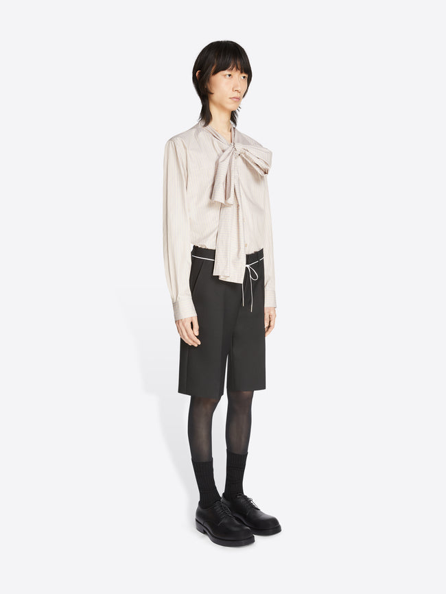 Person wearing a beige blouse with a bow and black pants on a white background