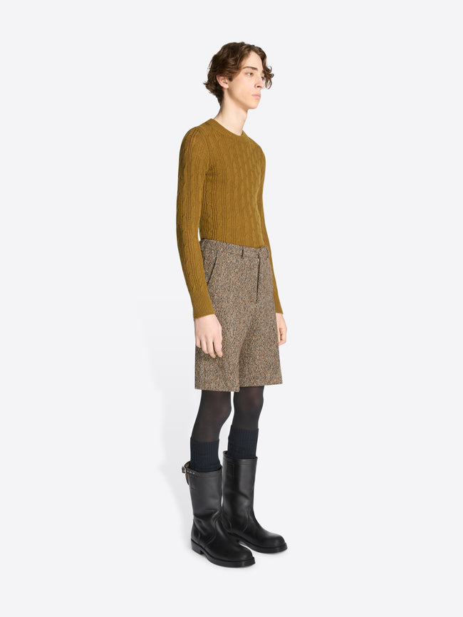 Person wearing a mustard sweater, patterned skirt, and black boots on a white background