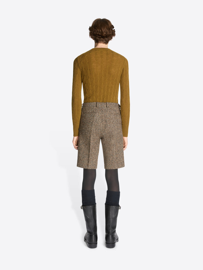 Person wearing a mustard sweater, brown patterned pants, and black boots on a white background