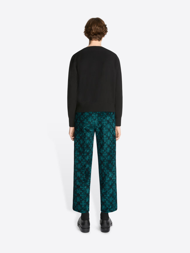 Person wearing a black sweater and patterned pants on a white background