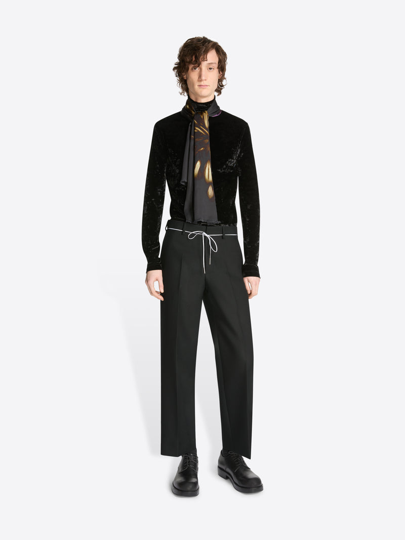 Person wearing a black velvet jacket, black pants, and a black shirt with a gold tie on a white background