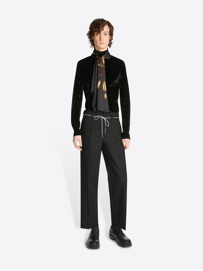 Person wearing a black velvet jacket, black pants, and a black shirt with a gold tie on a white background