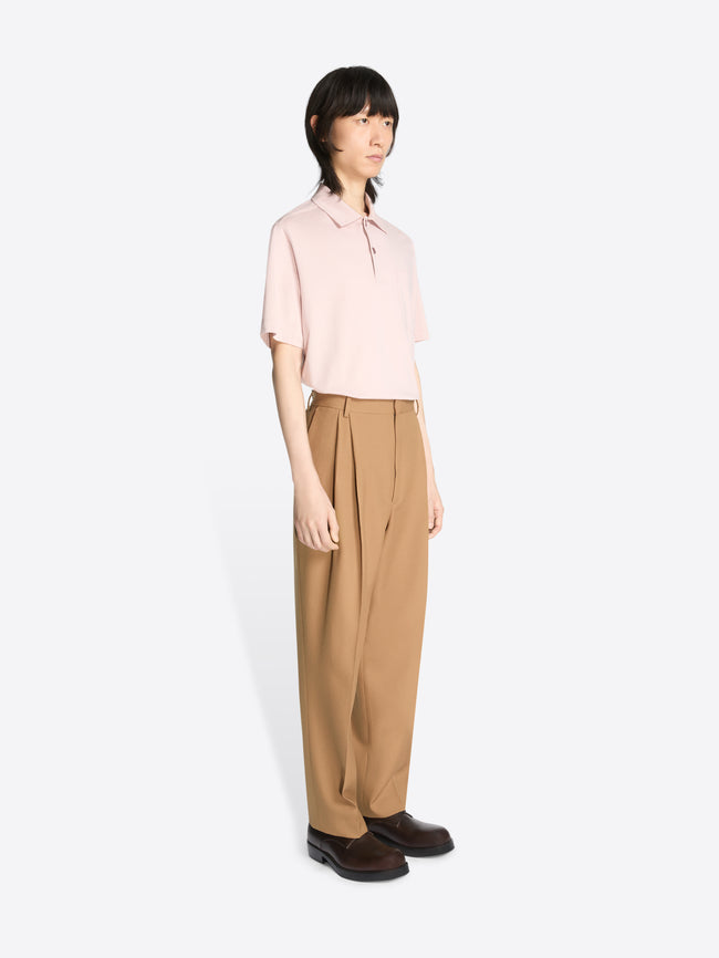 Model wearing a light pink colored shirt and a pair of a colored pleated wool pants on a white background