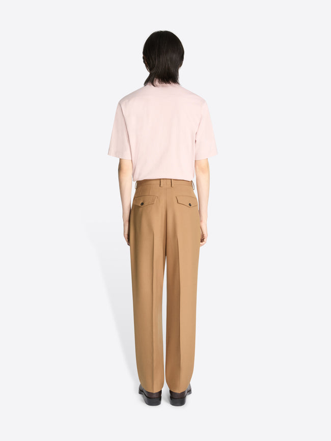 Backside of a model wearing a light pink colored shirt and a pair of a colored pleated wool pants on a white background