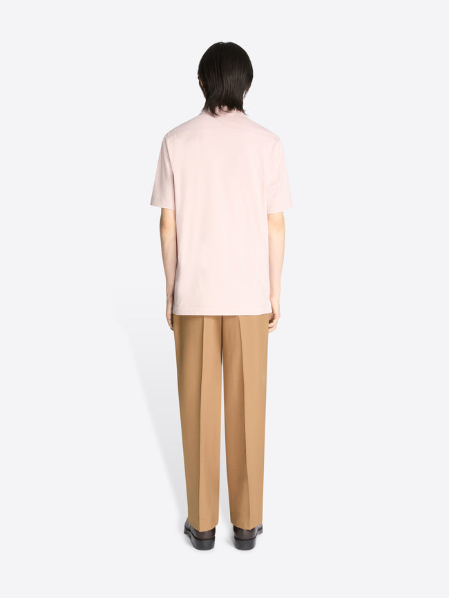 Backside of a model wearing a pale pink cotton polo shirt and beige pants on a white background