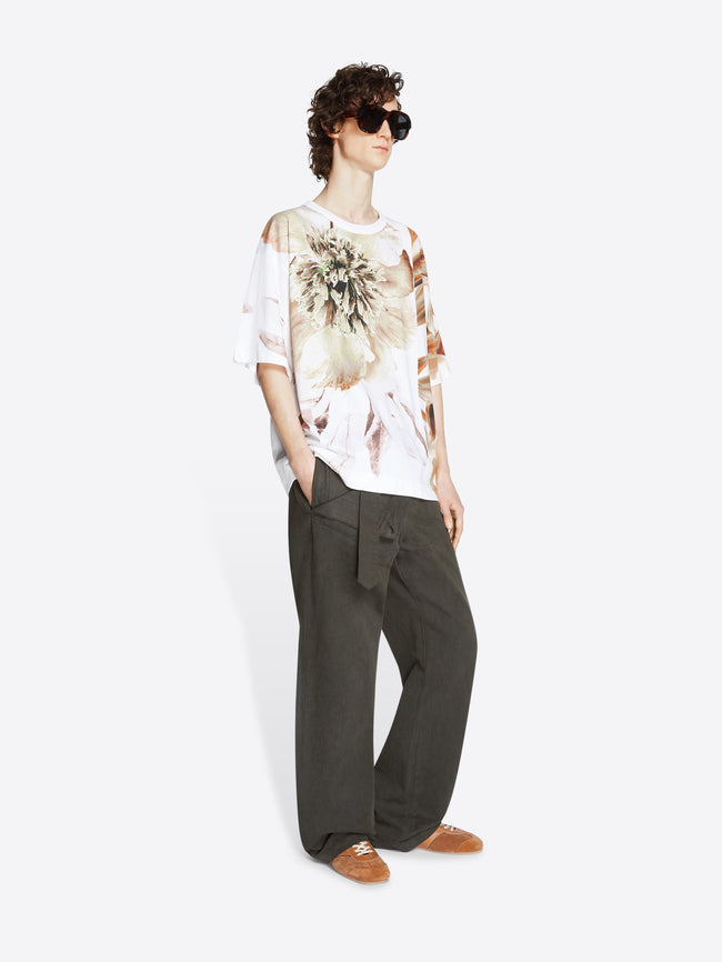 Model wearing an ocra colored oversized tee with flower print and dark grey pants on a white background