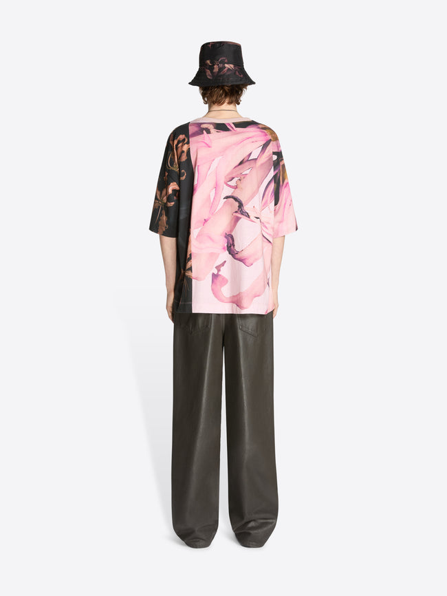 Backside of a model wearing floral pale pink oversized tee with black accent and black coated pants on a white background