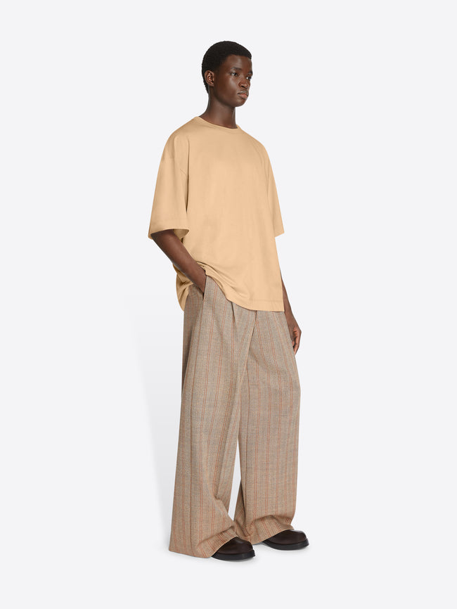 Model wearing a beige colored oversized tee and light brown pants on a white background