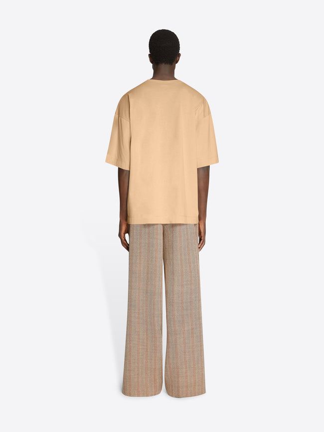Backside of a model wearing a beige colored oversized tee and light brown pants on a white background