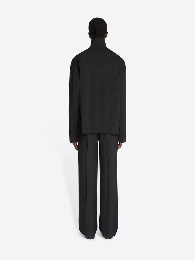 Backside of a model wearing a black, lace-up collar tee with long sleeves and a pair of black pants on a white background