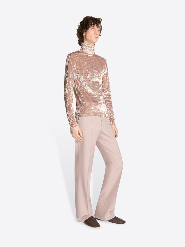 Model wearing a rose colored velvet turtleneck tee and light rose pants on a white background
