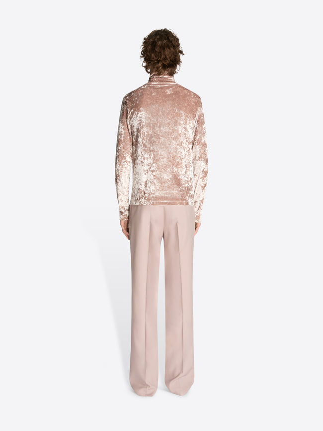 Backside of a model wearing a rose colored velvet turtleneck tee and light rose pants on a white background