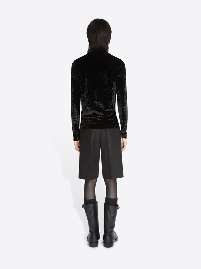Backside of a model wearing a black velvet turtleneck tee and black shorts on a white background