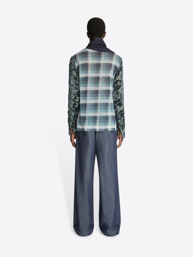 Backside of a model wearing a turquoise check pattern printed mesh tee with green patterned sleeves and a pair of denim pants on a white background