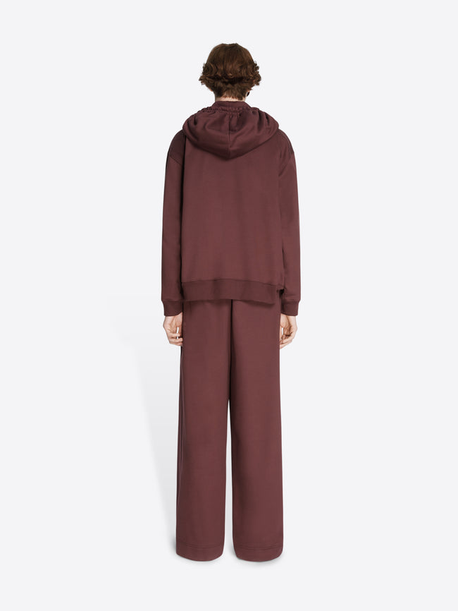Backside of a model wearing a burgundy loose fit hoodie and matching sweatpants on a white background