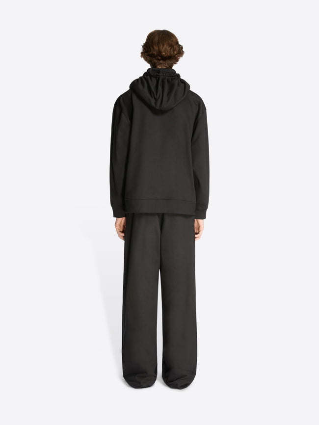 Backside of a model wearing a black loose fit hoodie and matching sweatpants on a white background