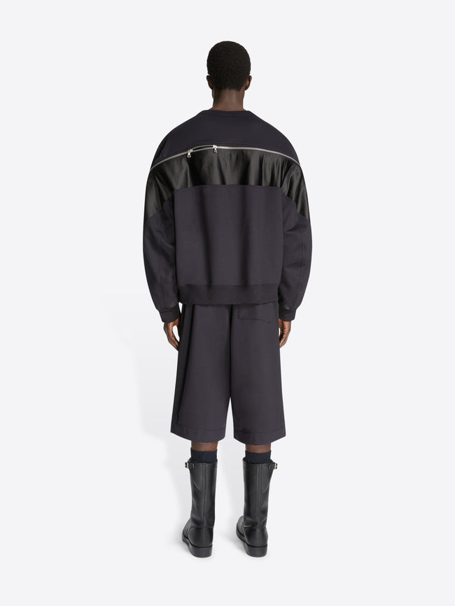 Backside of a model wearing dark grey shorts and a navy colored sweatshirt with contrast panels and zip detailing on a white background