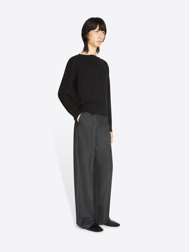Model wearing a pair of dark grey pants and a black cashmere sweater with front pocket on a white background