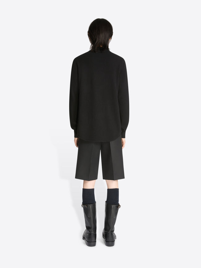 Backside of a model wearing a pair of black shorts and a black cashmere polo shirt with front pocket on a white background