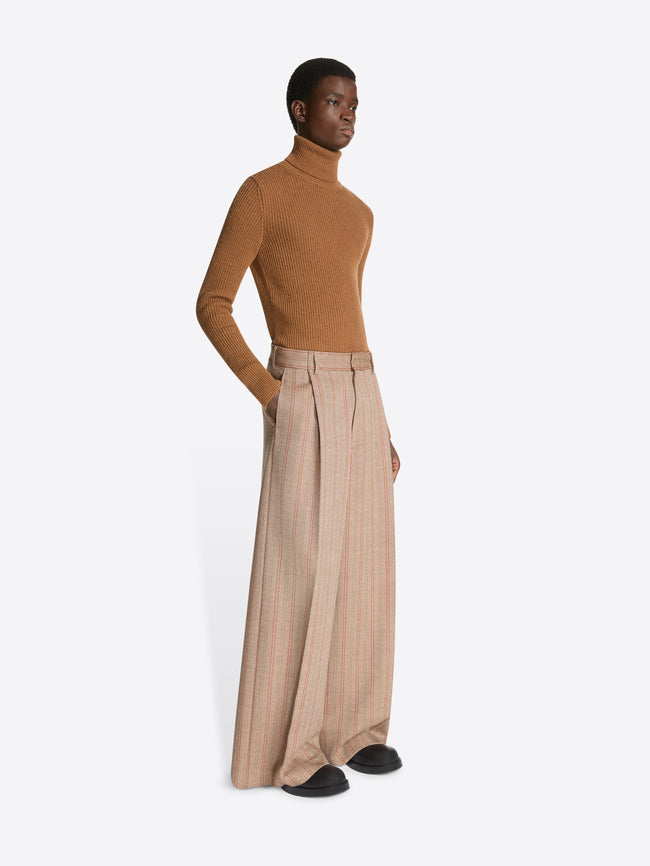 Model wearing a brown colored wool rib sweater and a pair of light brown striped pants on a white background