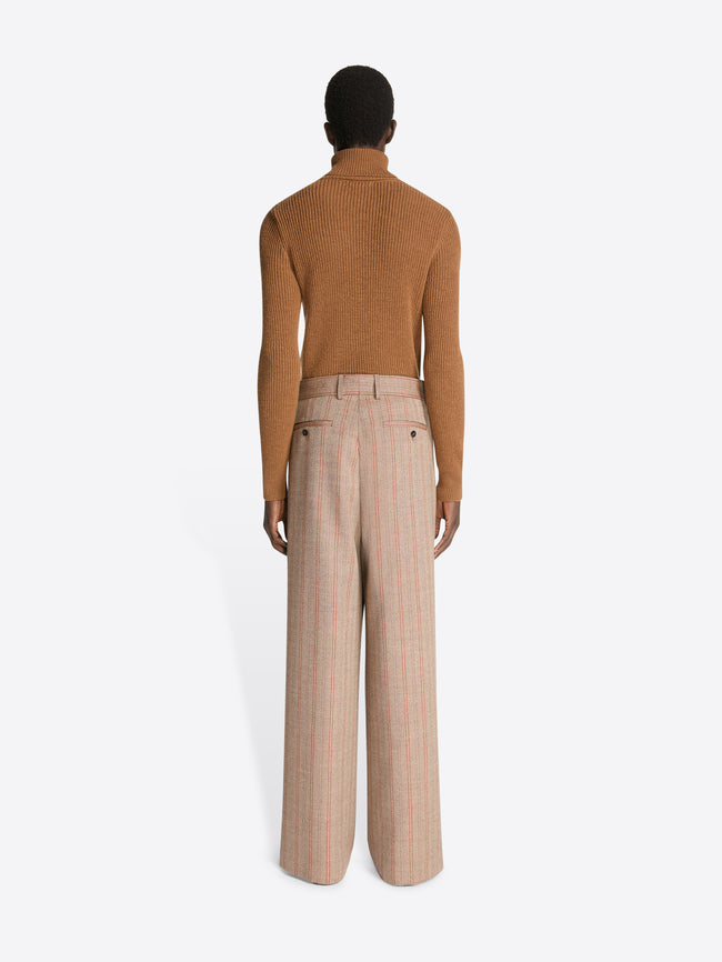 Backside of a model wearing a brown colored wool rib sweater and a pair of light brown striped pants on a white background