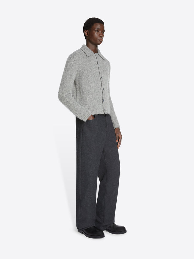 Model wearing a pair of dark grey pants and a light grey cropped wool cardigan on a white background