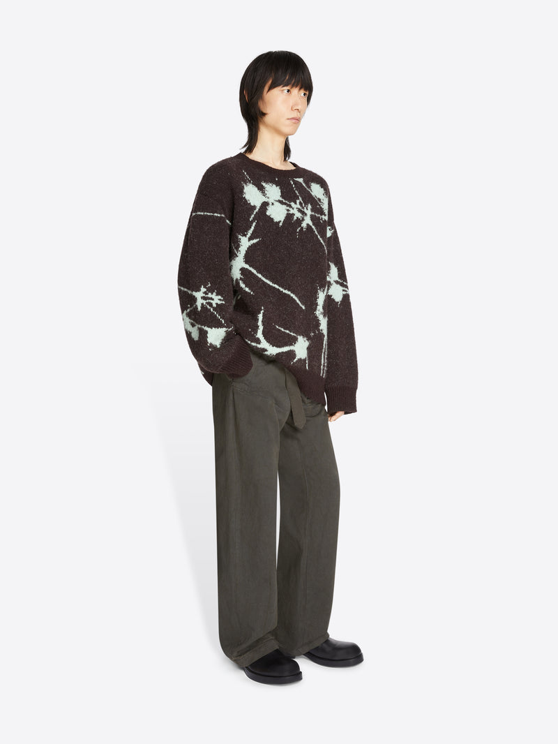 Person wearing a dark sweater with a floral pattern and gray pants on a white background